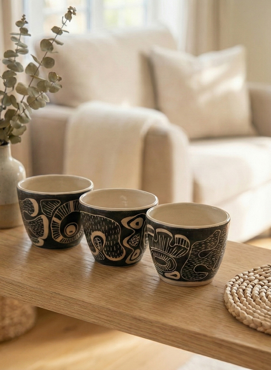 Three hand-carved black and white tea cups on an oak shelf