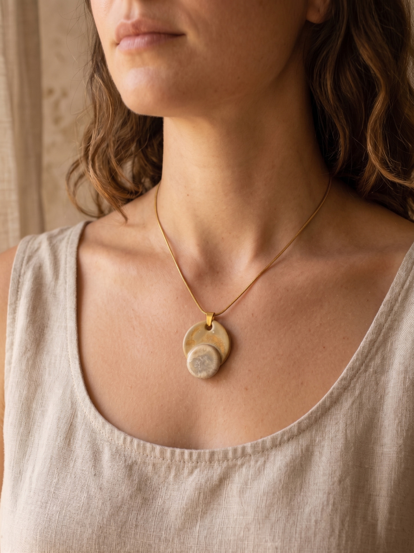 Eclipse pendant necklace in glazed stoneware and gold, worn on a linen top
